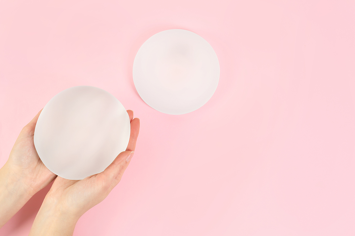 Woman holding silicone implant for breast augmentation on color