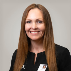 Portræt af en kvindelig medarbejder hos Cerix i sort uniform, smilende mod kameraet. Billedet viser primært ansigt og langt hår og illustrerer ansigtsbehandlinger som Botox. Navneskilt med foto er synligt. Nærbillede med naturligt smil og velplejet hud signalerer tryghed og professionalisme.