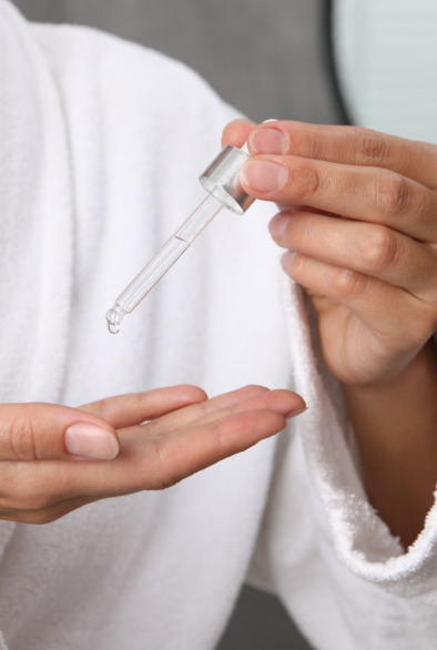 Woman applying cosmetic serum onto her hand indoors, closeup