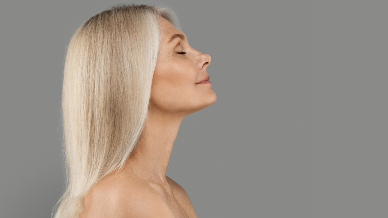Profile of beautiful mature woman with flawless skin standing with closed eyes