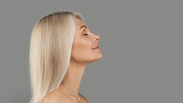 Profile of beautiful mature woman with flawless skin standing with closed eyes