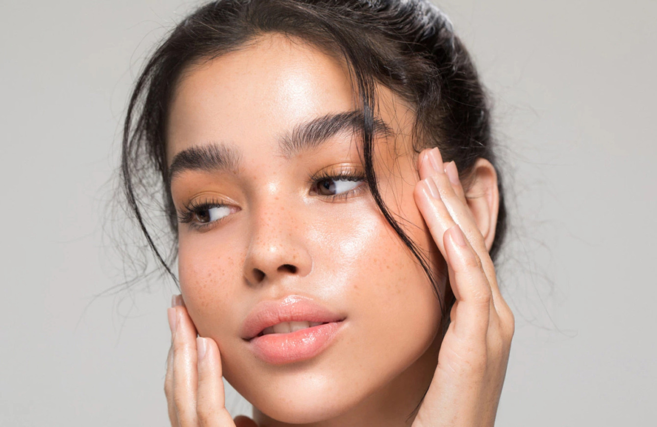 Nærbillede af ungt kvindeligt ansigt med glat, fugtig hud og let fregner, hænder der berører kinderne. Billedet bruges af Cerix til at illustrere ansigtsbehandlinger som Botox og filler ved ansigtet, med fokus på naturligt udseende, klinisk præcision og sikkerhed.