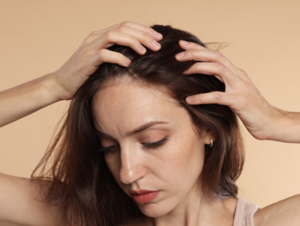 Nærbillede af en kvinde med fregner, der kører fingrene gennem sit brune hår og undersøger sin hovedbund. Hendes blik er vendt nedad. Billedet illustrerer fokus på hår hos Cerix, hvor der tilbydes professionel vejledning og effektive behandlinger mod hårtab og forbedring af hårets sundhed.