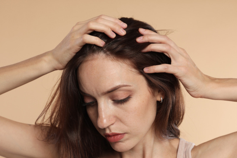 Nærbillede af en kvinde med fregner, der kører fingrene gennem sit brune hår og undersøger sin hovedbund. Hendes blik er vendt nedad. Billedet illustrerer fokus på hår hos Cerix, hvor der tilbydes professionel vejledning og effektive behandlinger mod hårtab og forbedring af hårets sundhed.