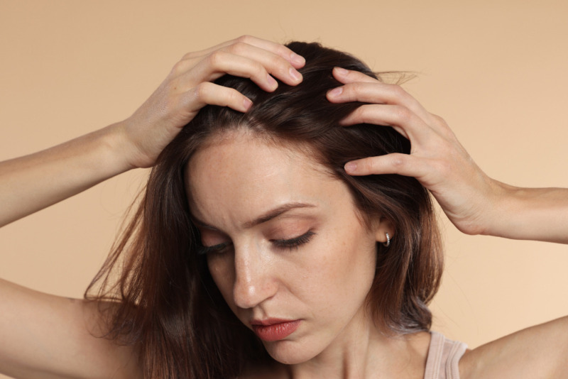 Nærbillede af en kvinde med fregner, der kører fingrene gennem sit brune hår og undersøger sin hovedbund. Hendes blik er vendt nedad. Billedet illustrerer fokus på hår hos Cerix, hvor der tilbydes professionel vejledning og effektive behandlinger mod hårtab og forbedring af hårets sundhed.