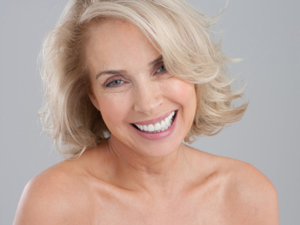 Nærbillede af en smilende moden kvinde med blondt hår og bare skuldre. Hun har en glat og ungdommelig hud i ansigtet og på halsen, hvilket kunne være et resultat af behandlinger hos Cerix som for eksempel Botox, fillers eller skinbooster.