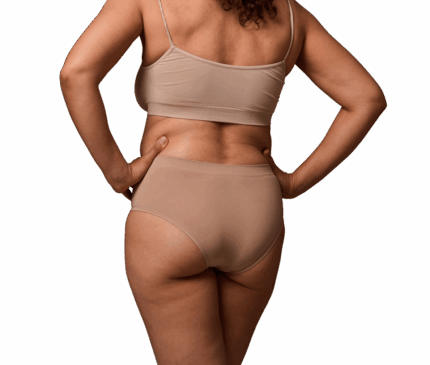 Billede af en kvinde set bagfra, iført beige top og trusser, med hænderne placeret i siden på en hvid baggrund. Dette billede illustrerer kropsområder som ryg og balder, der er relevante for behandlinger som kropsformning eller Brazilian Butt Lift (BBL) hos Cerix for at opnå en mere defineret silhuet.
