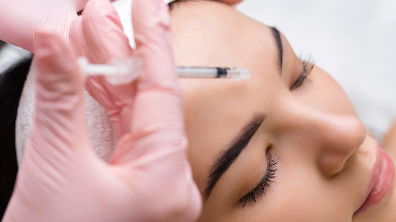 Nærbillede af en klient, der modtager en kosmetisk injektion, sandsynligvis Botox eller filler, i panden hos Cerix. En behandler med lyserøde handsker administrerer forsigtigt sprøjten i ansigtet for at udglatte huden.