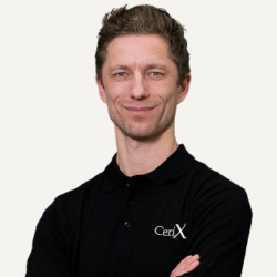 Cerix-medarbejder står foran neutral baggrund iført sort Cerix-polo, smilende med armene over kors. Portræt af en mandligt ansigt og overkrop, professionelt og imødekommende, der repræsenterer klinikken og ansigtsbehandlinger som Botox og filler. Bruges til Cerix’ informations- og patientmateriale.