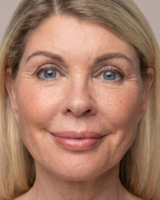 Portræt af en smilende, voksen kvinde med blondt hår og synlige fine linjer omkring øjne, pande og mund.