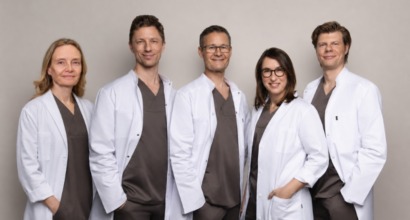 Professionelt gruppeportræt af fem læger og behandlere fra Cerix, iført hvide kitler over gråt arbejdstøj og stående foran en neutral baggrund. Billedet viser Cerix som virksomhed og det medicinske team.
