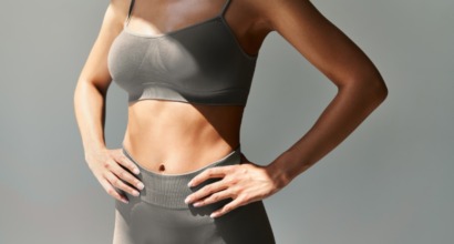 Illustrativt foto af en kvindes overkrop iført gråt træningstøj, hvor den bare, slanke mave og talje er i fokus. Billedet relaterer til maveplastik (abdominoplastik), en behandling hos Cerix, som virksomhed inden for kosmetisk kirurgi, samt behandlinger, der former og opstrammer kroppens maveområde.